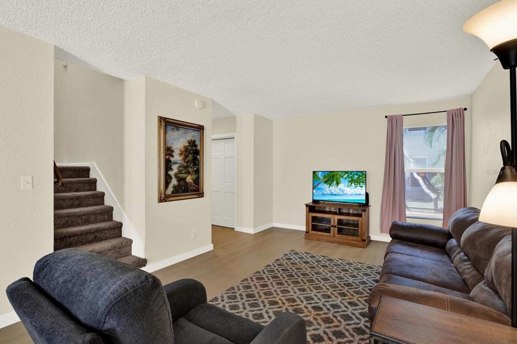 A living room features brown carpeted stairs, light wood flooring, a television, and a sofa — 1799 N HIGHLAND AVENUE UNIT 53, CLEARWATER, FL
