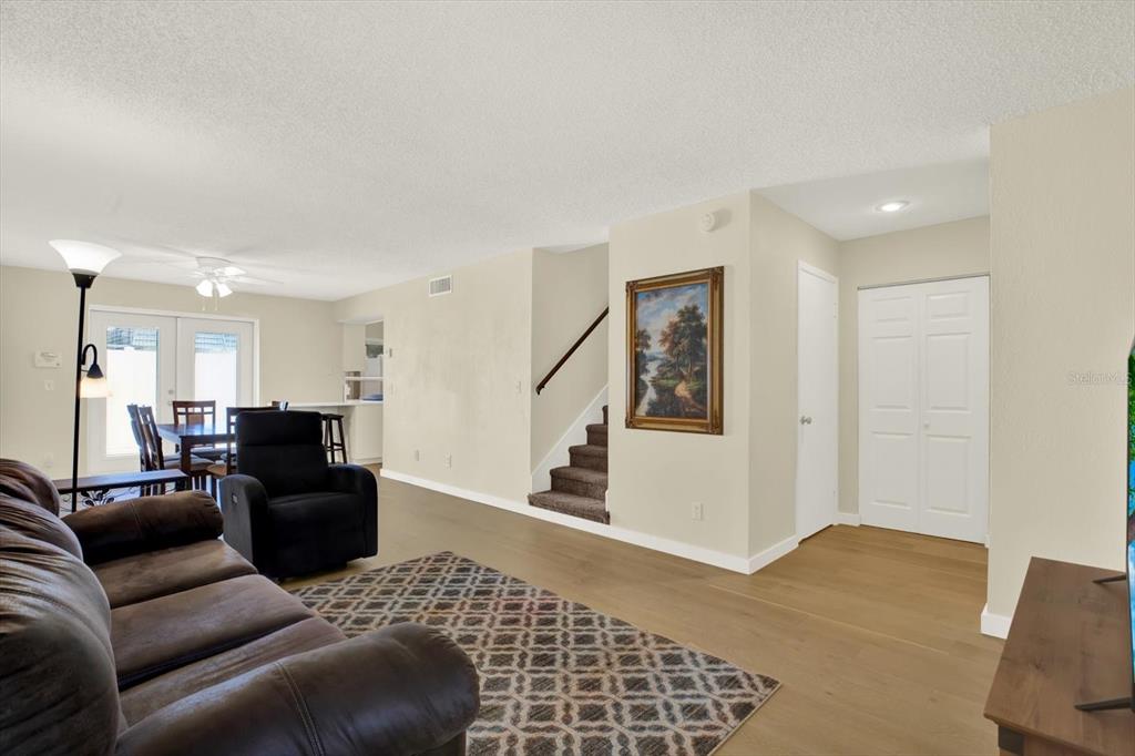 A living room with light wood flooring, a dark sofa, a recliner, and a staircase — 1799 N HIGHLAND AVENUE UNIT 53, CLEARWATER, FL