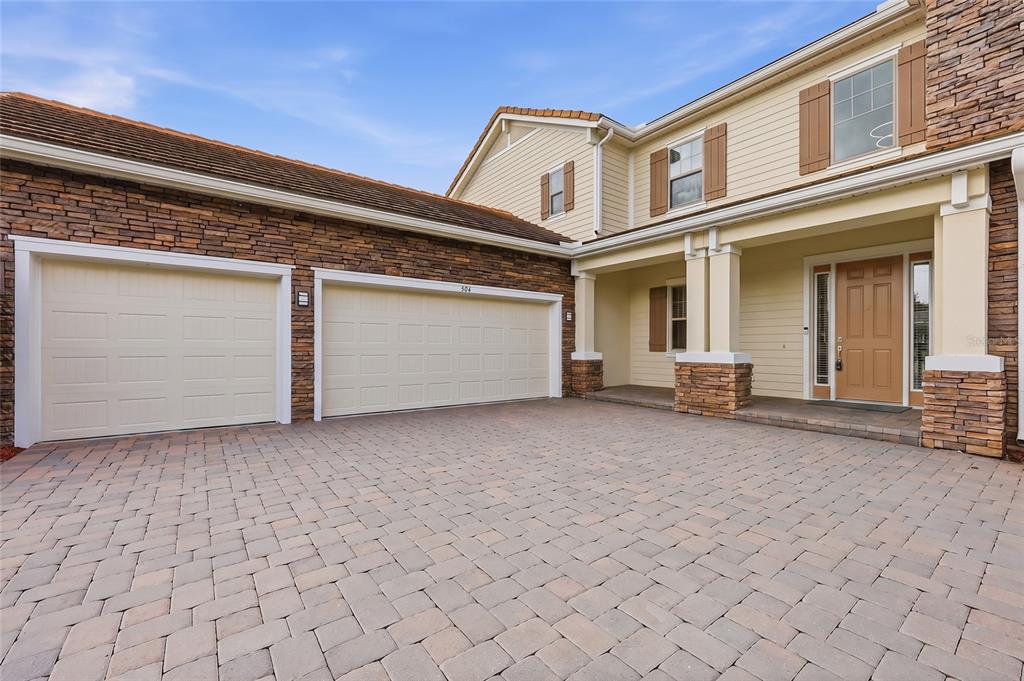 A two-story house exterior features a stone facade, a paved driveway, and a three-car garage — 504 CINDER POINT, SANFORD, FL
