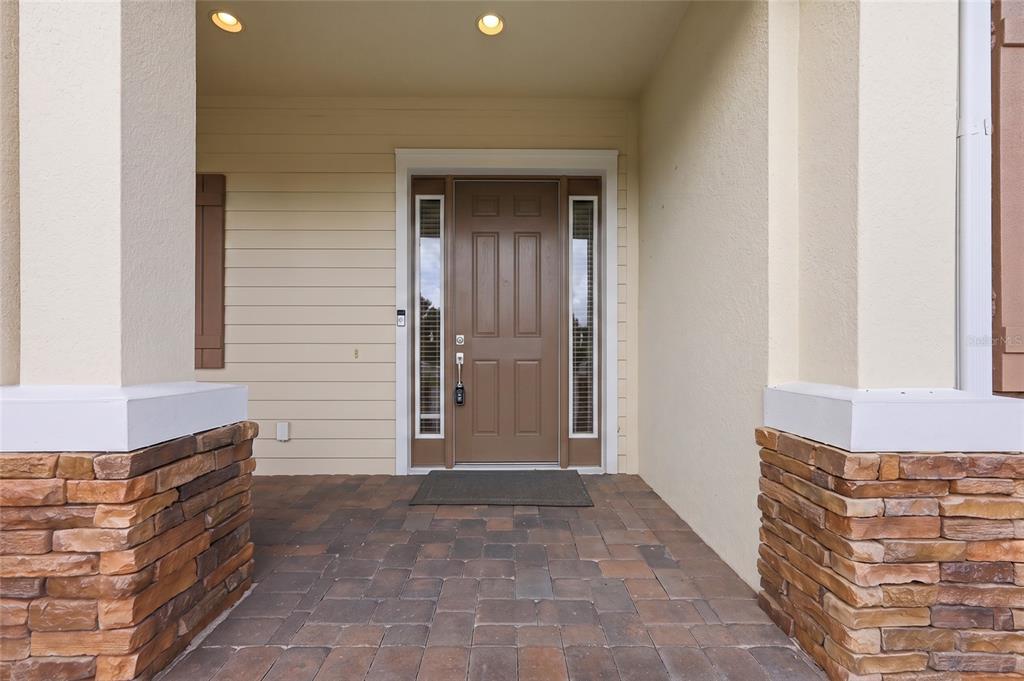 A covered entryway features a brown front door with sidelights, stone pillars, and paver flooring — 504 CINDER POINT, SANFORD, FL