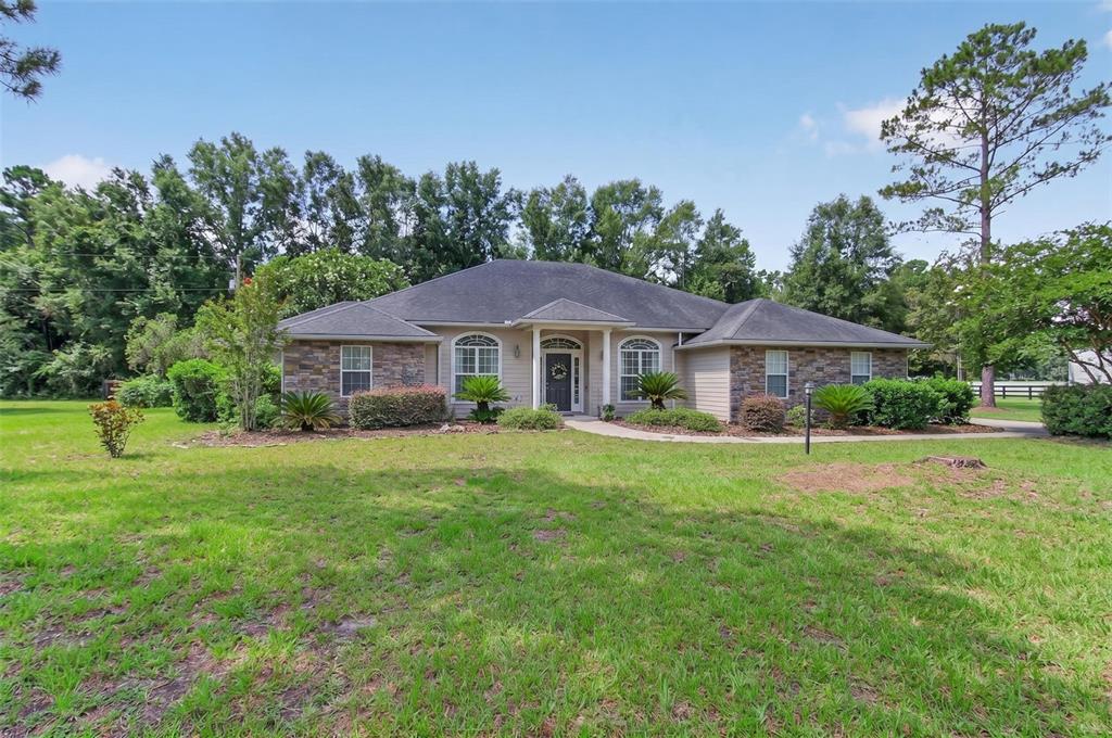 A single-story house with stone veneer accents, a dark roof, and a large front lawn — 24865 NW 155TH AVENUE, HIGH SPRINGS, FL