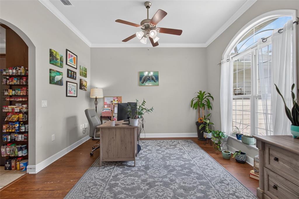 A home office with a wooden desk, gray area rug, ceiling fan, and large arched window — 24865 NW 155TH AVENUE, HIGH SPRINGS, FL