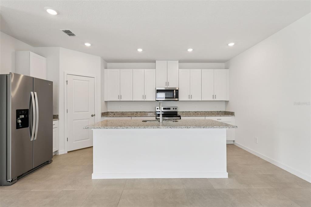 A modern kitchen features white cabinetry, granite countertops, a central island, and stainless steel appliances — 77 WANDERING CREEK WAY, PALM COAST, FL
