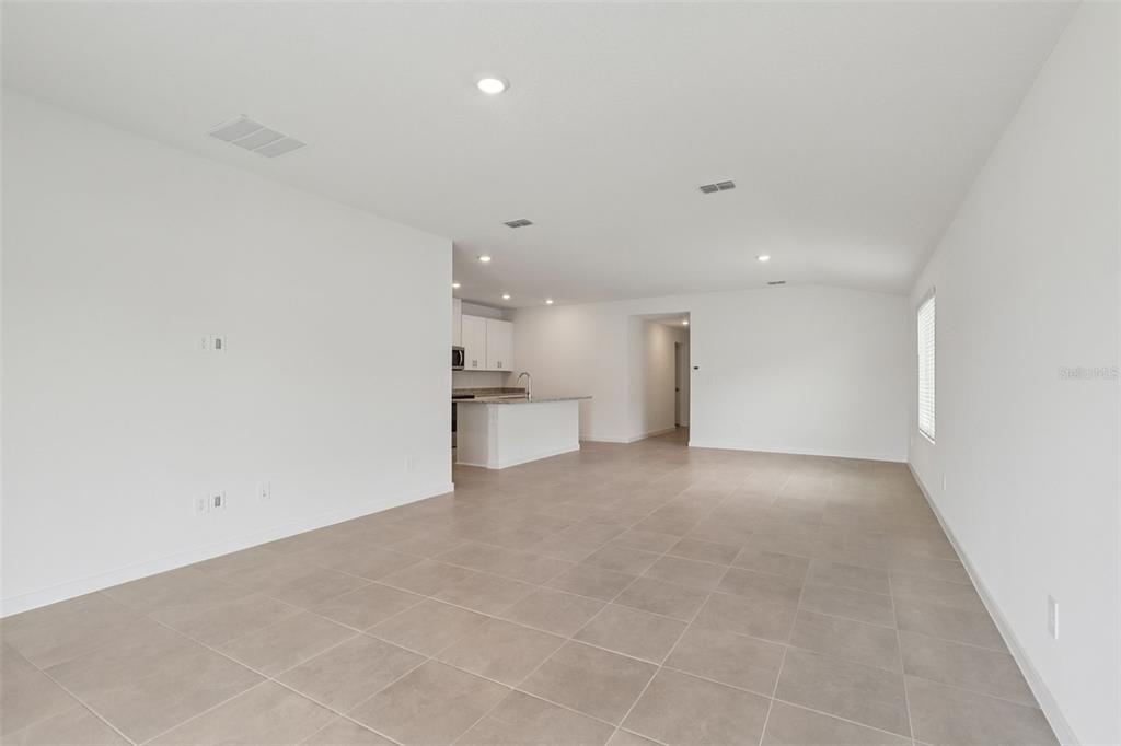 An open-concept living area with light tile flooring leads to a kitchen with white cabinets — 77 WANDERING CREEK WAY, PALM COAST, FL