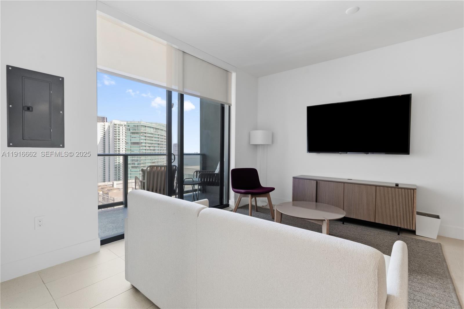 A modern living room features a white sofa, a wall-mounted television, and a balcony view — 159 NE 6th St # 4713, Miami FL 33132, MIAMI, FL