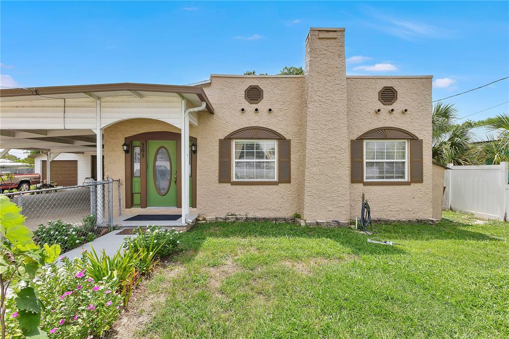 A tan stucco house features a green front door, a chimney, and a metal carport — 205 TENNESSEE STREET, HAINES CITY, FL