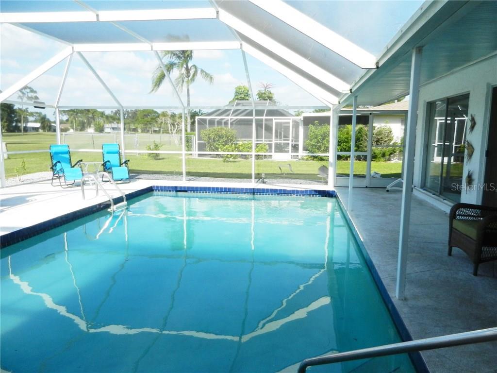 A screened-in swimming pool with blue lounge chairs sits on a patio overlooking a yard — 98 CADDY ROAD, ROTONDA WEST, FL