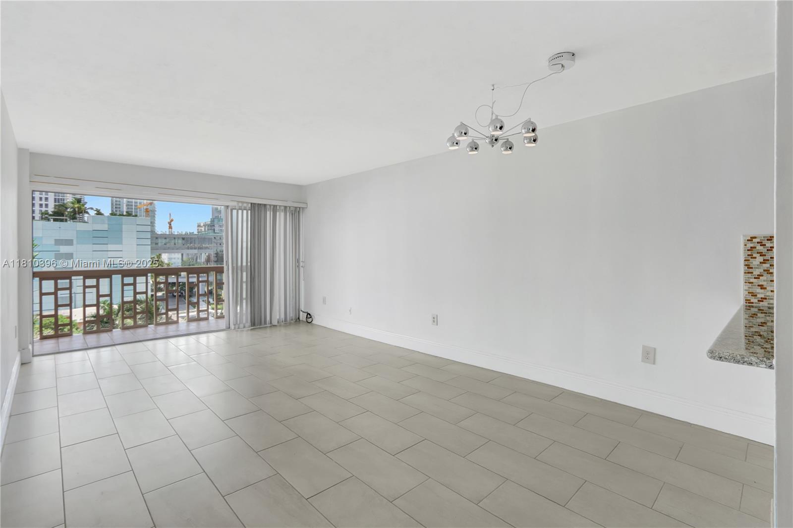 An empty living room features light tile flooring, white walls, a modern chandelier, and a balcony — 600 NE 25th St, Miami FL 33137, MIAMI, FL