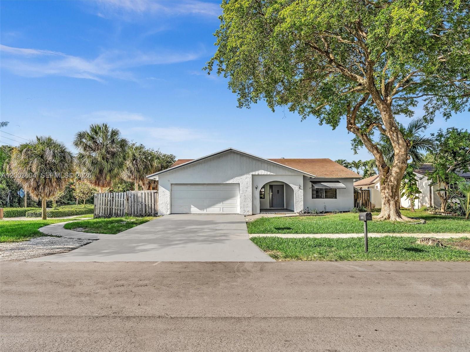 A single-story white house with a two-car garage and a large tree in front — DANIA BEACH, FL