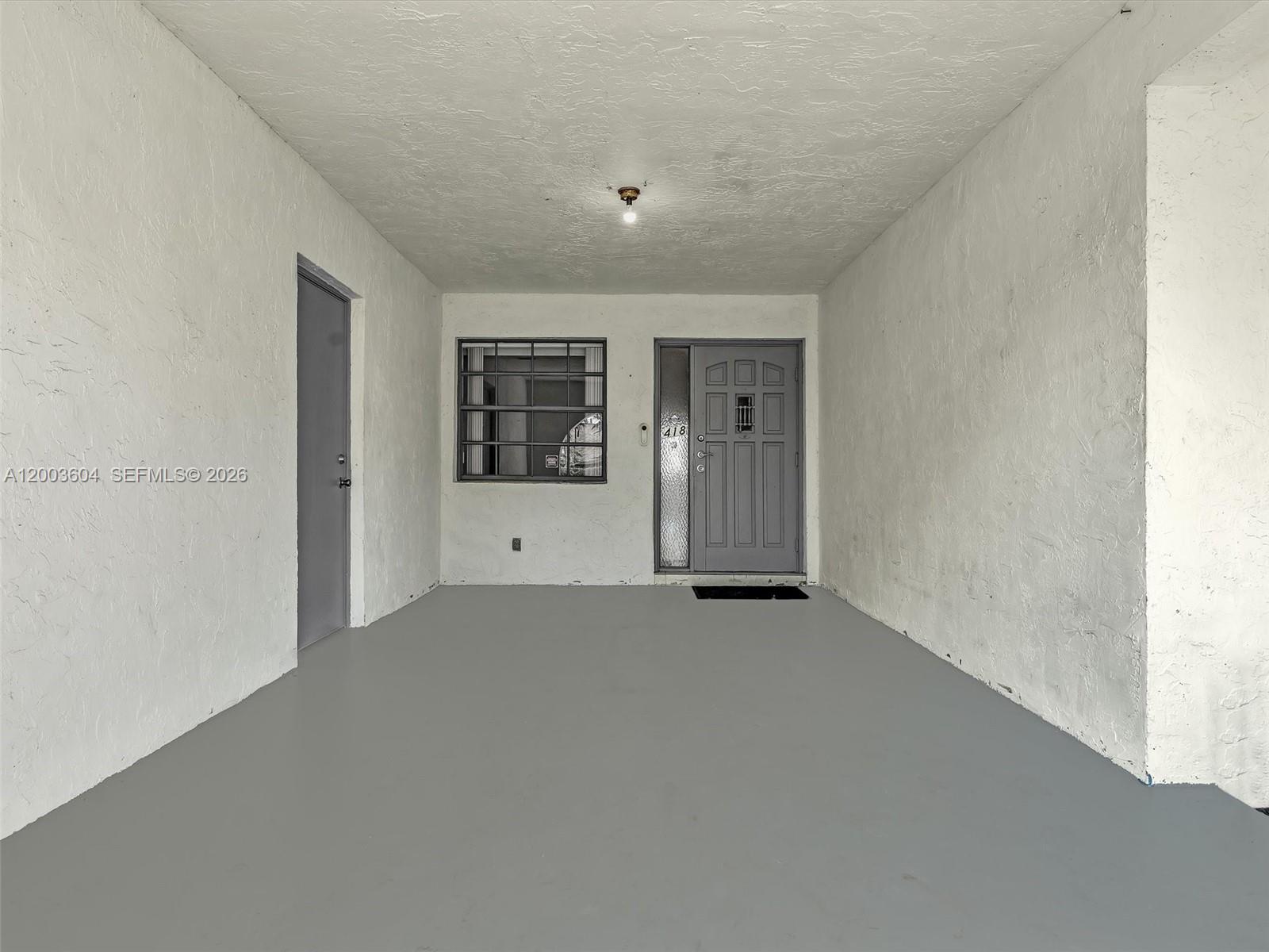 A covered entryway features a gray door, a window with security bars, and painted concrete floors — DANIA BEACH, FL