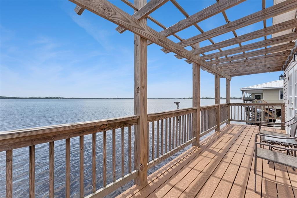 A wooden deck with a pergola overlooks a large lake under a clear blue sky — 1849 MOORINGS COURT, CLERMONT, FL