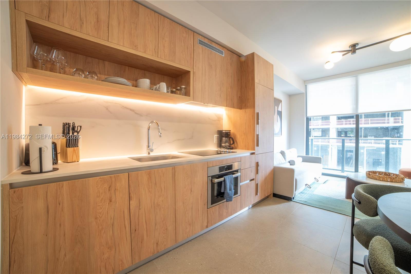 A modern kitchen features light wood cabinets, a marble backsplash, and an integrated oven — 11 NE 6TH # 1403, Miami FL 33132, MIAMI, FL