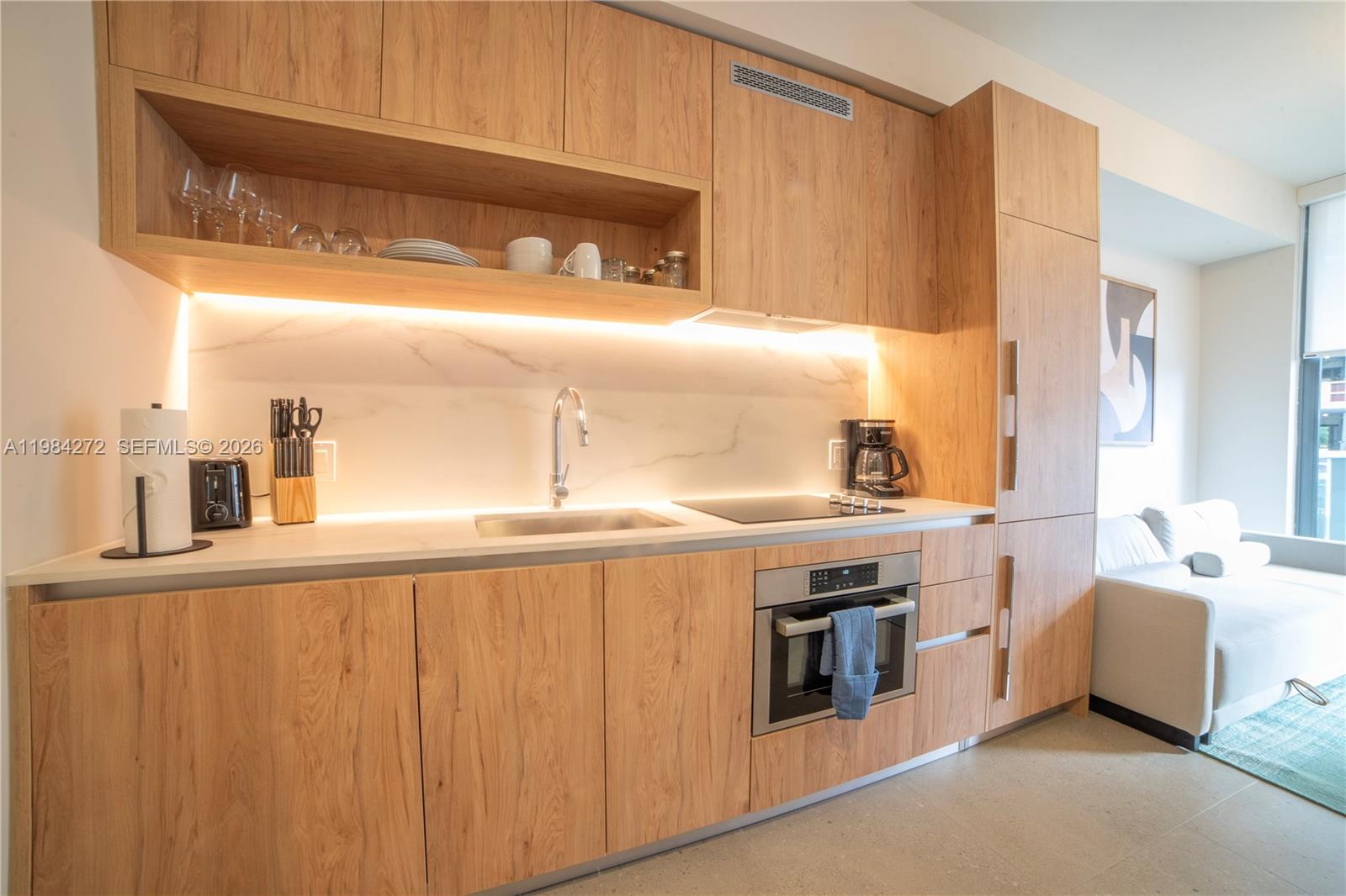 A modern kitchen features light wood cabinetry, a marble backsplash, and integrated stainless steel appliances — 11 NE 6TH # 1403, Miami FL 33132, MIAMI, FL