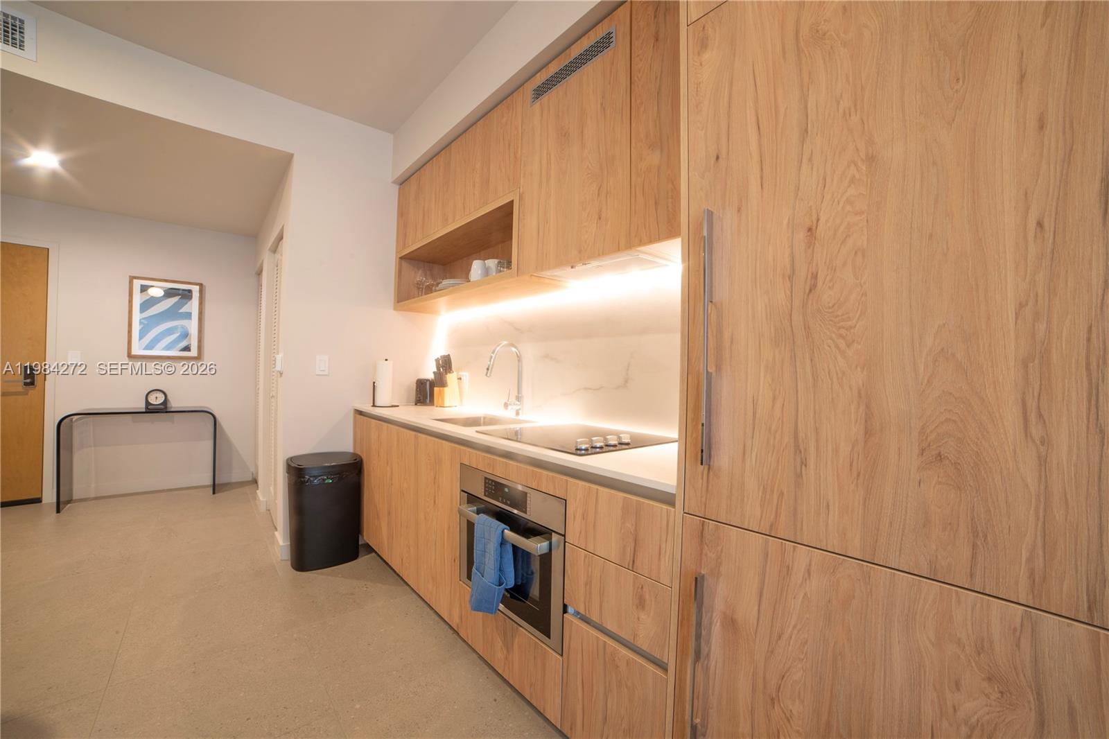 A modern kitchen features light wood cabinetry, a white countertop, and integrated stainless steel appliances — 11 NE 6TH # 1403, Miami FL 33132, MIAMI, FL