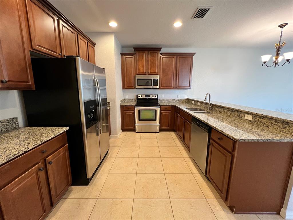 A kitchen with wood cabinets, stainless steel appliances, granite countertops, and light-colored tile flooring — 1853 GARDEN SAGE DRIVE, OVIEDO, FL