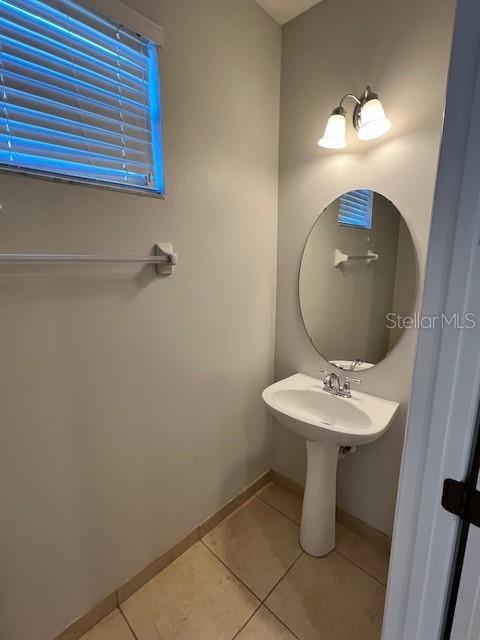 A small half bathroom features a pedestal sink, a round mirror, and a window with blinds — 1853 GARDEN SAGE DRIVE, OVIEDO, FL