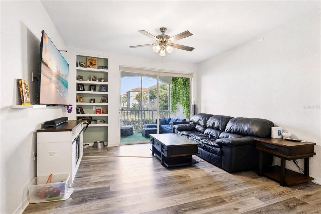 A living room features wood-look flooring, a black leather sofa, a television, and built-in shelving — 2615 MAITLAND CROSSING WAY UNIT 104, ORLANDO, FL