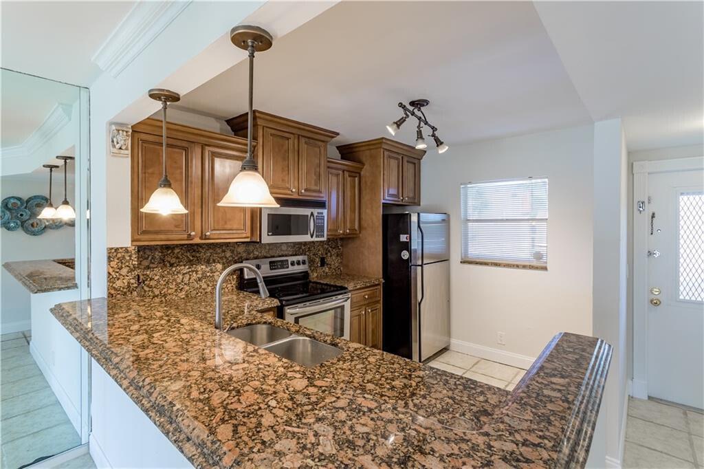 A kitchen features brown wooden cabinets, granite countertops, stainless steel appliances, and a breakfast bar — 2800 Fiore Way # 2060, Delray Beach FL 33445, DELRAY BEACH, FL