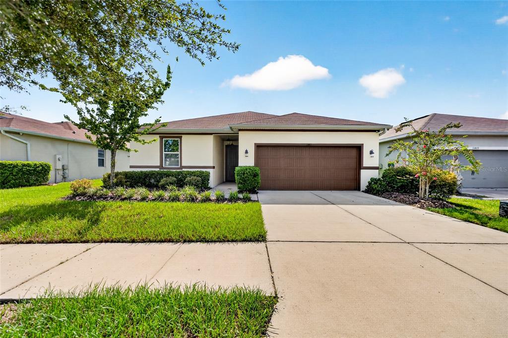 A single-story suburban house with a tan exterior, a brown garage door, and a driveway — 11411 TANGLE BRANCH LANE, GIBSONTON, FL