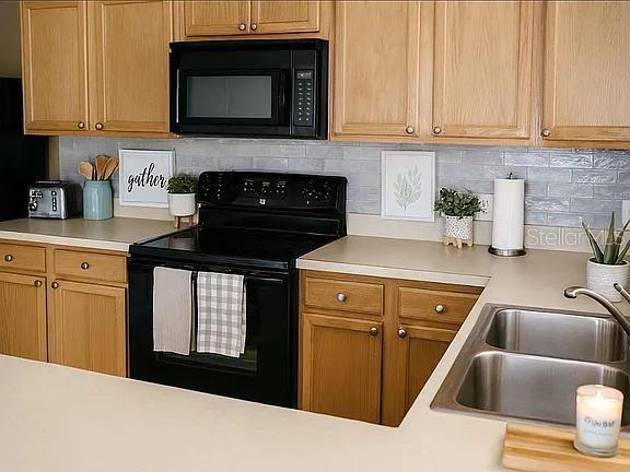 A kitchen features oak cabinets, a black microwave and stove, and a stainless steel sink — 2503 HASSONITE STREET, KISSIMMEE, FL