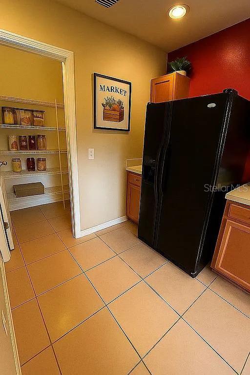 A kitchen features a walk-in pantry, a black refrigerator, and light-colored tile flooring — 2503 HASSONITE STREET, KISSIMMEE, FL