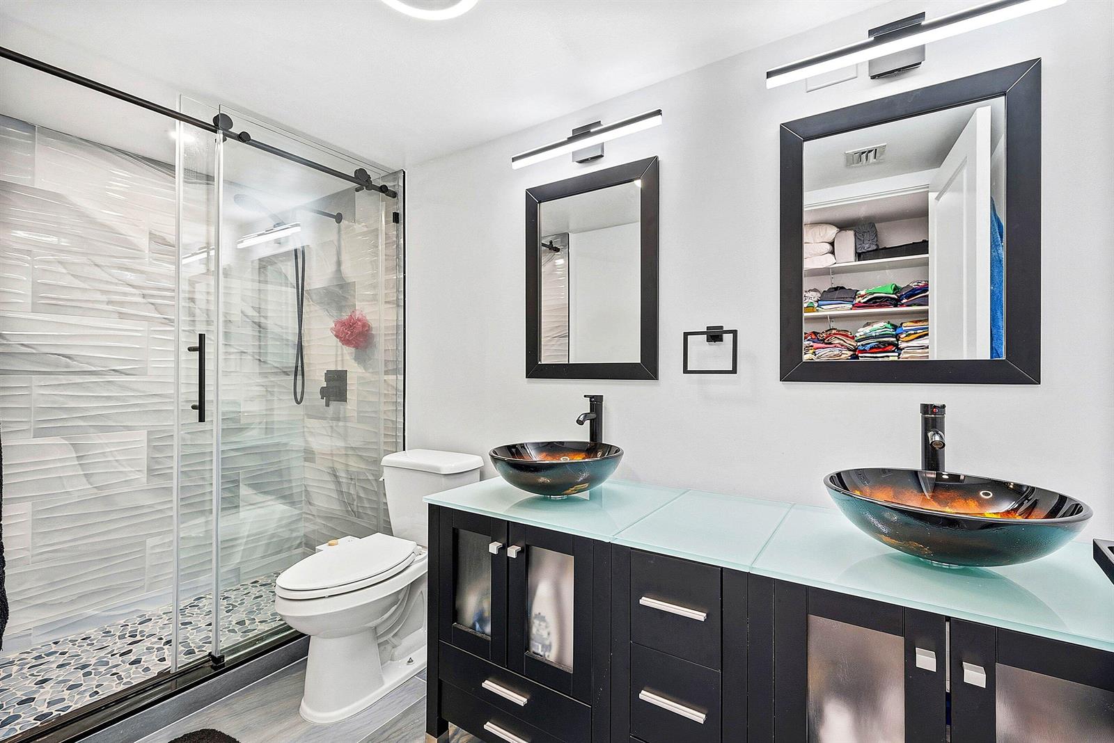 A bathroom features a glass-enclosed shower, a double vanity with vessel sinks, and black cabinetry — 18 Royal Palm Way Way # 109, Boca Raton FL 33432, BOCA RATON, FL