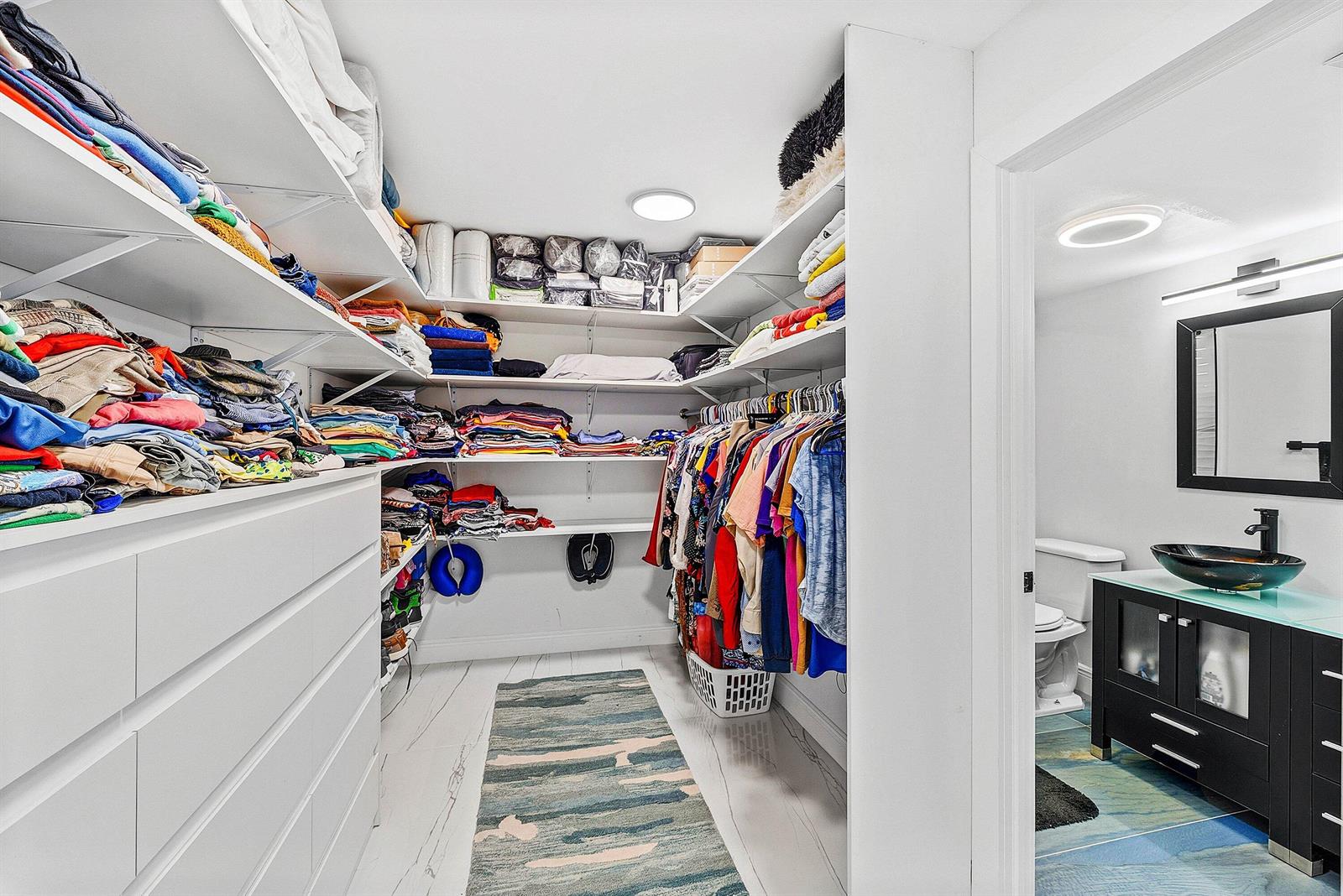 A walk-in closet with white shelving and drawers leads into a bathroom with a vanity — 18 Royal Palm Way Way # 109, Boca Raton FL 33432, BOCA RATON, FL