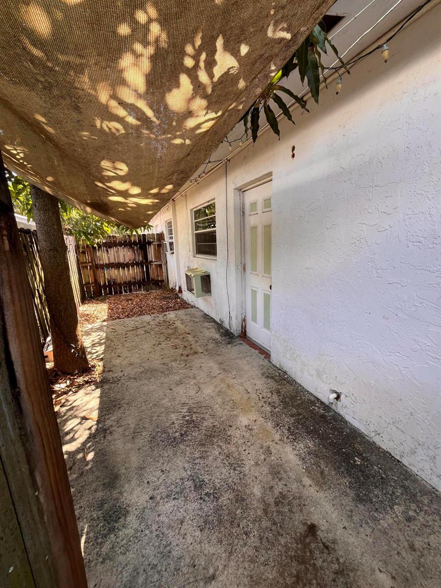 A concrete patio area features a shade sail, a white door, and a window unit — 1304 NE 4th Street, Pompano Beach FL 33060, POMPANO BEACH, FL