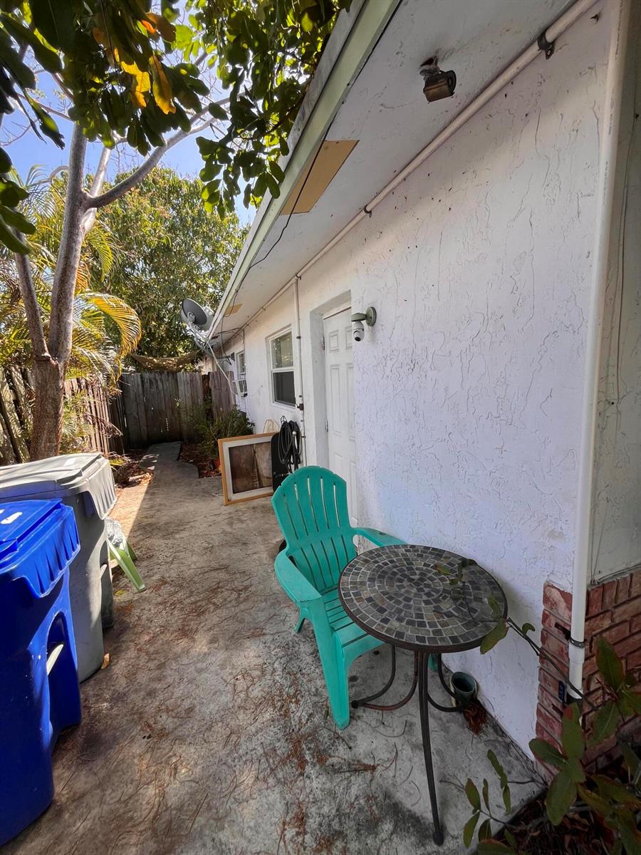A concrete patio area features a teal chair, a small mosaic table, and trash bins — 1304 NE 4th Street, Pompano Beach FL 33060, POMPANO BEACH, FL