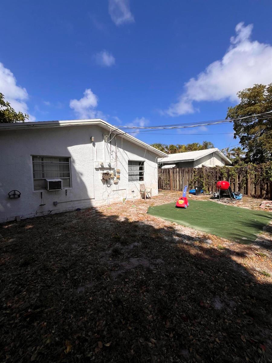 A backyard with a white house, a patch of artificial turf, and a wooden fence — 1304 NE 4th Street, Pompano Beach FL 33060, POMPANO BEACH, FL