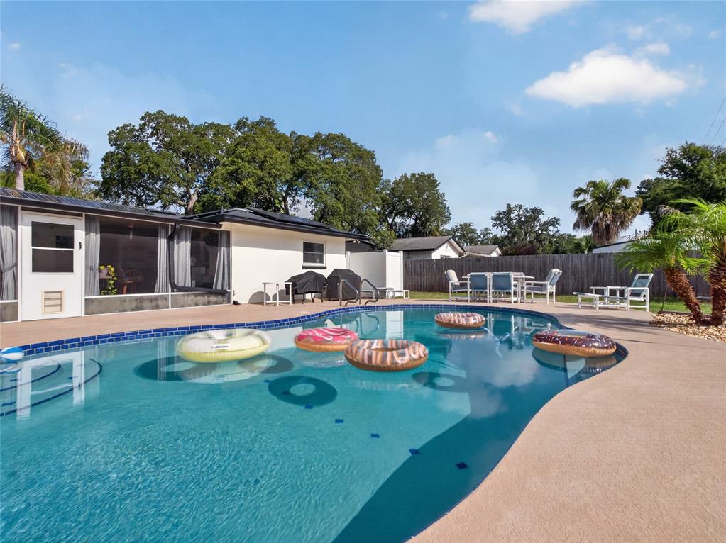 A backyard swimming pool with several inflatable floats sits beside a house with a patio — 127 ROSE BRIAR DRIVE, LONGWOOD, FL