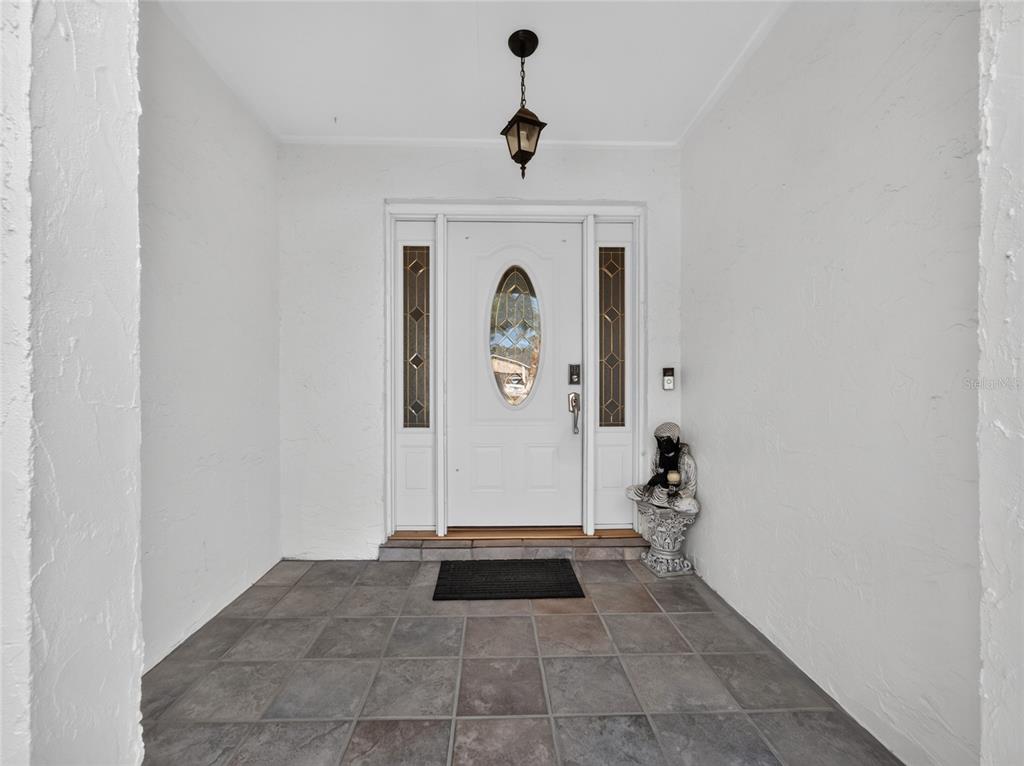 A white front door with sidelights and a hanging lantern sits on a tiled porch — 127 ROSE BRIAR DRIVE, LONGWOOD, FL