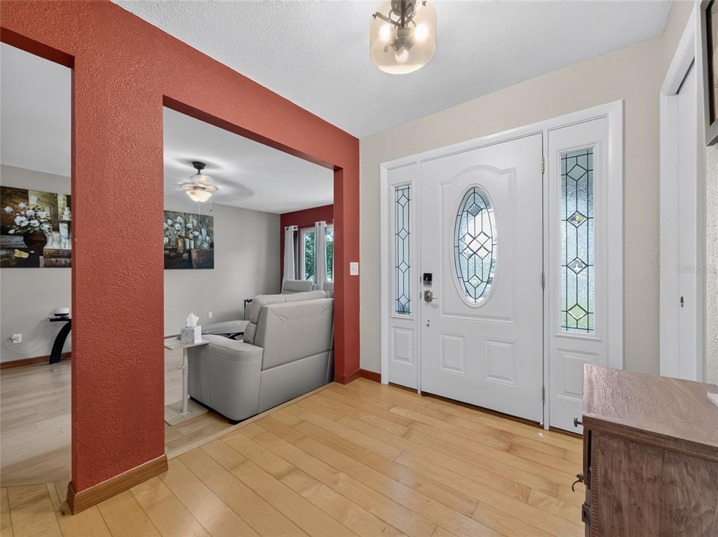 An entryway with light wood flooring, a white front door, and a red-painted wall opening — 127 ROSE BRIAR DRIVE, LONGWOOD, FL