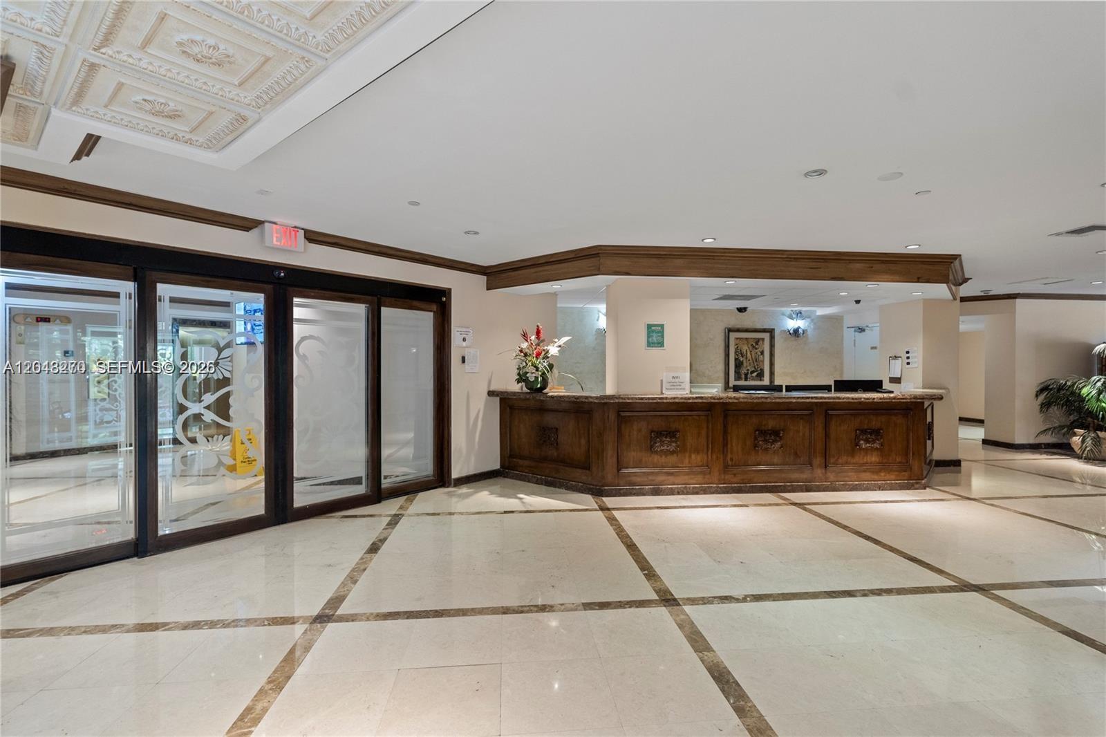 A hotel lobby features a wooden reception desk, marble floors, and glass entrance doors — AVENTURA, FL