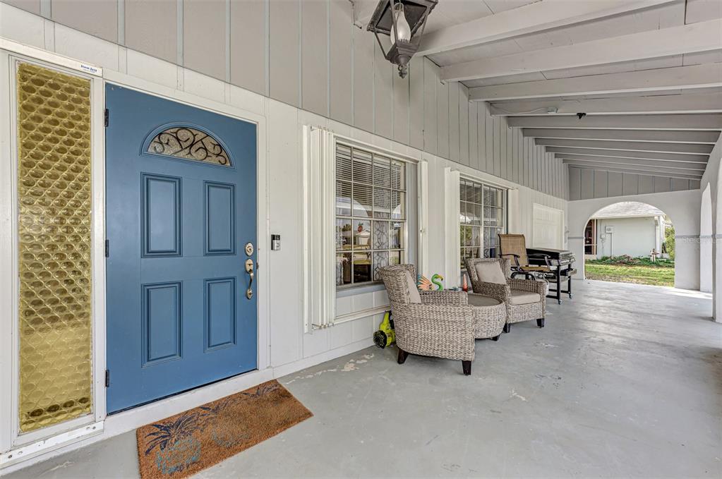 A covered porch features a blue front door, wicker chairs, and a concrete floor — 13479 NEWPORT AVENUE, PORT CHARLOTTE, FL