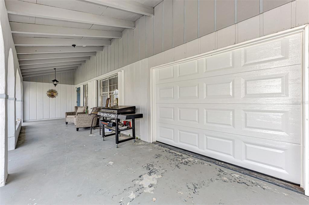 A covered patio features a white garage door, a grill, and outdoor seating — 13479 NEWPORT AVENUE, PORT CHARLOTTE, FL