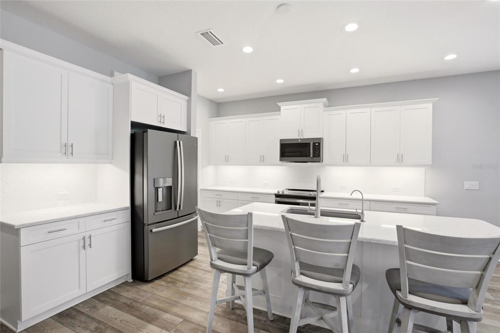 A modern kitchen features white cabinetry, a stainless steel refrigerator, and a central island — 7545 RIDGELAKE CIRCLE, BRADENTON, FL