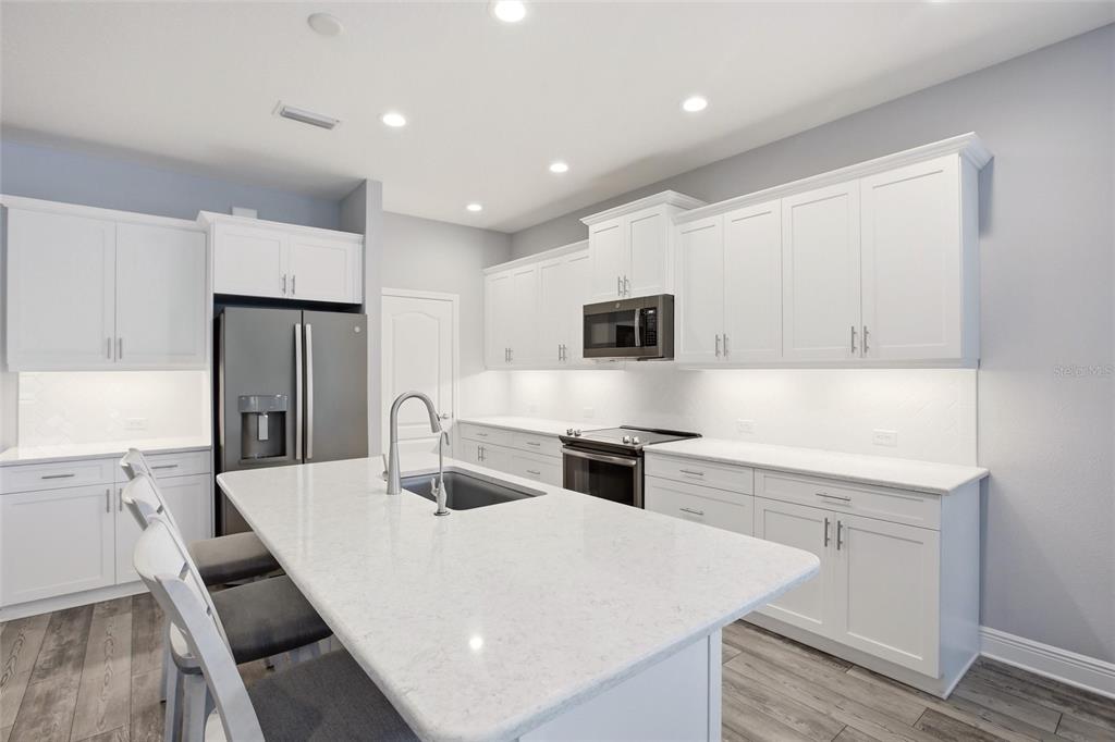 A modern kitchen features white cabinetry, a large quartz island, and stainless steel appliances — 7545 RIDGELAKE CIRCLE, BRADENTON, FL