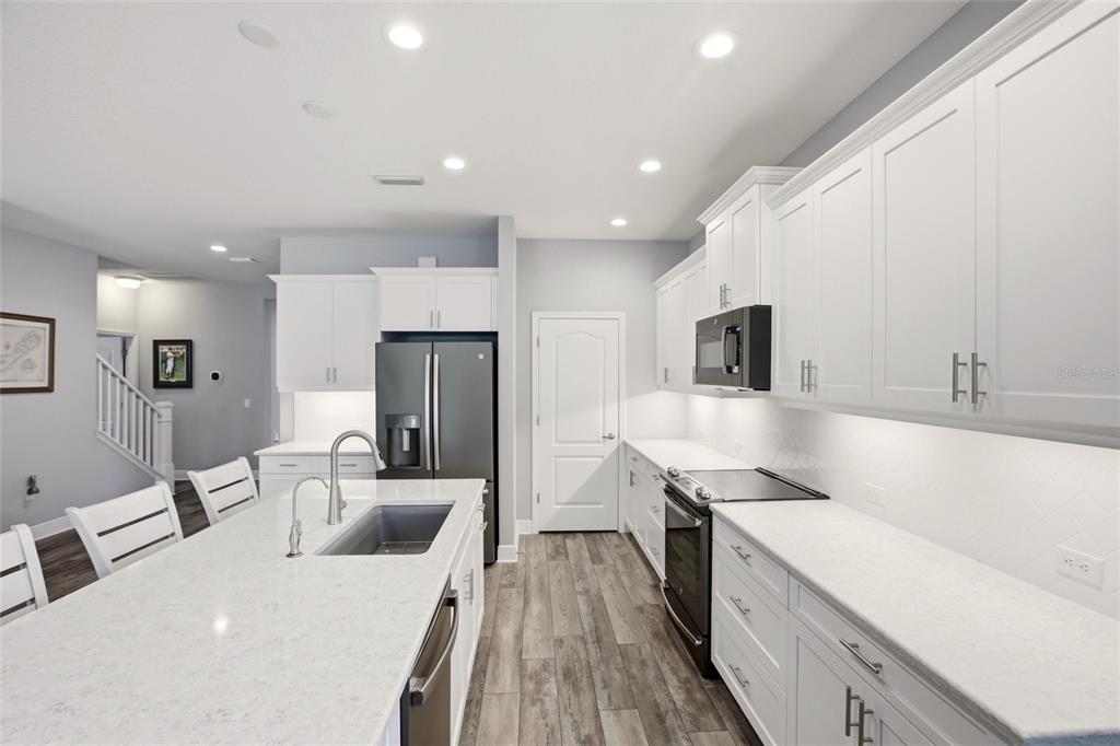 A modern kitchen features white cabinetry, quartz countertops, a large island, and stainless steel appliances — 7545 RIDGELAKE CIRCLE, BRADENTON, FL