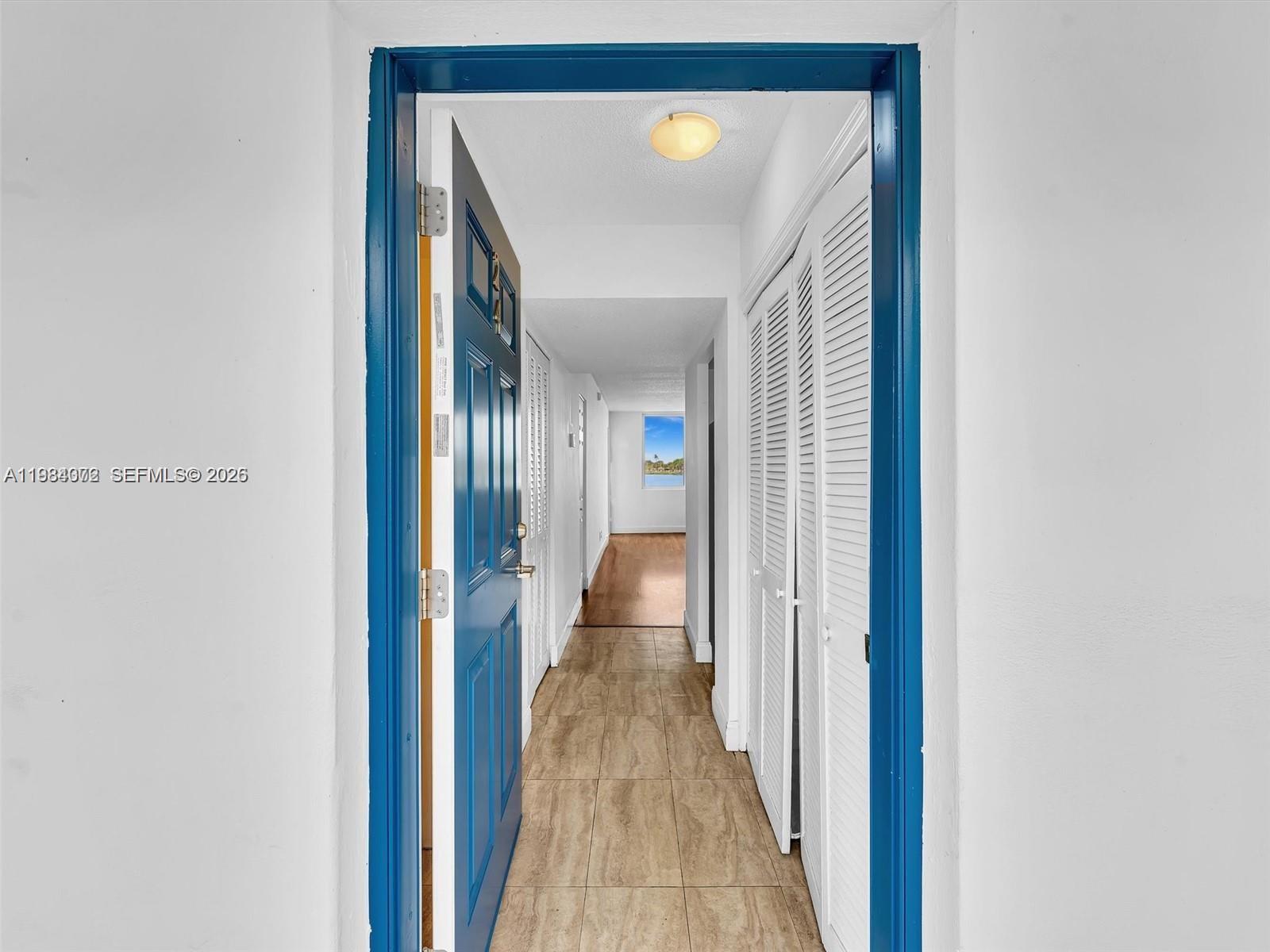 A blue door opens into a tiled hallway leading toward a window with a view — 1170 NE 191st St # 24, Miami FL 33179, MIAMI, FL