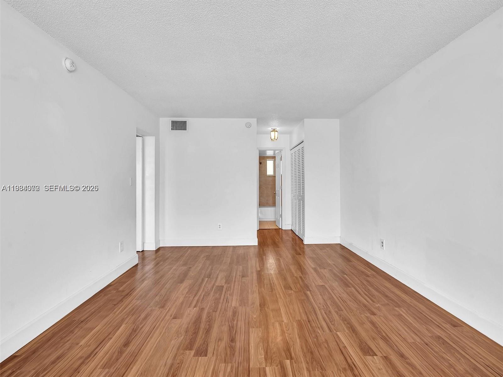 An empty room features white walls, wood-look flooring, and a doorway leading to a bathroom — 1170 NE 191st St # 24, Miami FL 33179, MIAMI, FL