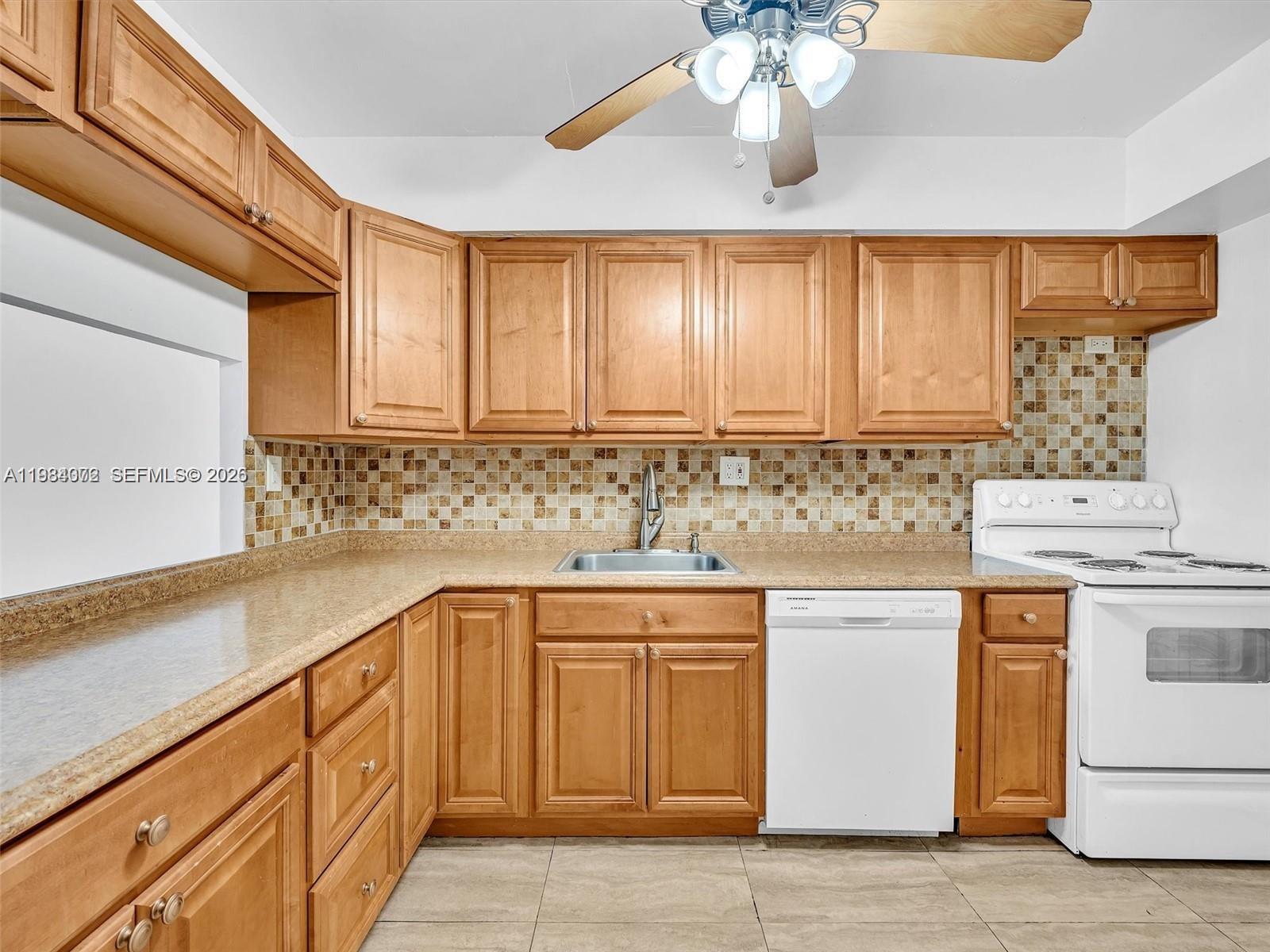 A kitchen features light wood cabinets, tan countertops, a tiled backsplash, and a white dishwasher — 1170 NE 191st St # 24, Miami FL 33179, MIAMI, FL