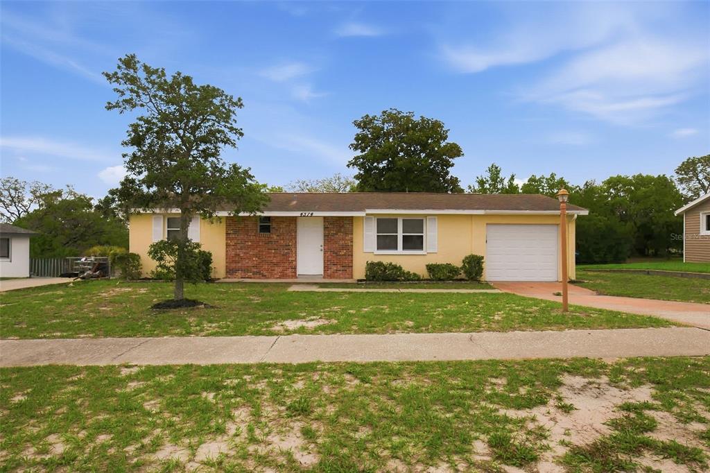A single-story yellow house with a brick entryway, a garage, and a front lawn — 4374 ORIOLE AVENUE, SPRING HILL, FL