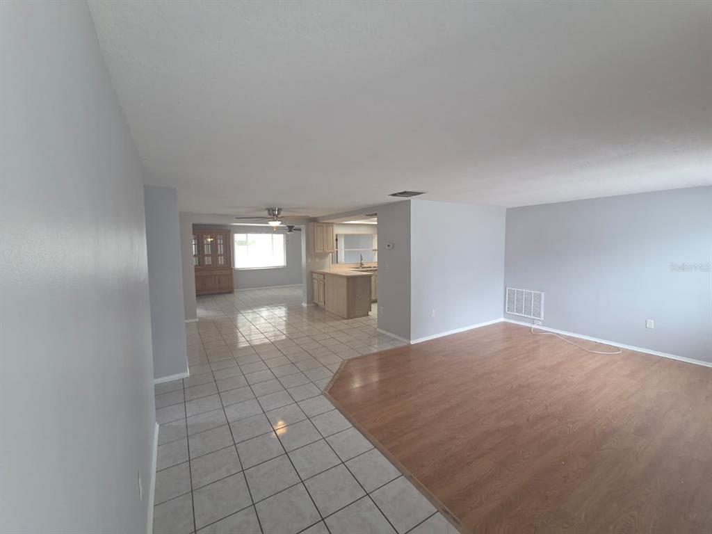 An open-concept living area features light-colored tile flooring, wood-look laminate flooring, and a kitchen — 3619 SPRINGFIELD DRIVE, HOLIDAY, FL