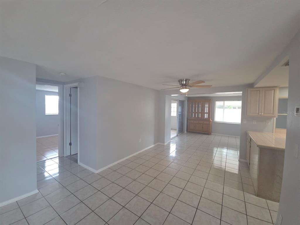 An open-concept living and dining area features light gray walls and beige tiled flooring — 3619 SPRINGFIELD DRIVE, HOLIDAY, FL