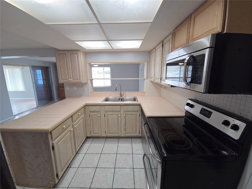 A kitchen features light wood cabinets, tiled countertops, a black stove, and a drop ceiling — 3619 SPRINGFIELD DRIVE, HOLIDAY, FL