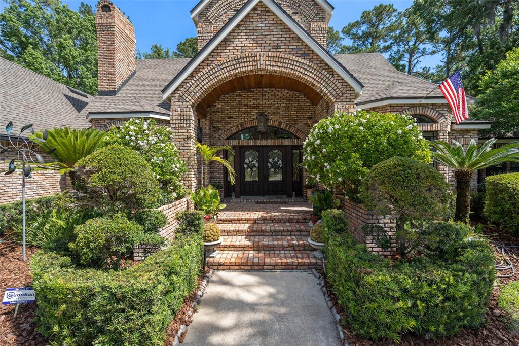 A brick house exterior features a covered arched entryway, a walkway, and landscaped front gardens — 2214 EARLEAF COURT, LONGWOOD, FL