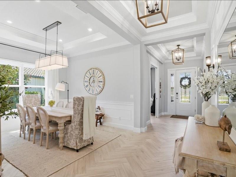 A dining room and entryway feature light wood herringbone floors, white wainscoting, and tray ceilings — 6243 PLATEAU COURT, BRADENTON, FL