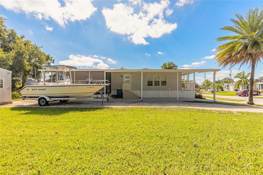 A single-story manufactured home with a boat parked on a paved driveway under a carport — 152 RED BASS LANE, EDGEWATER, FL