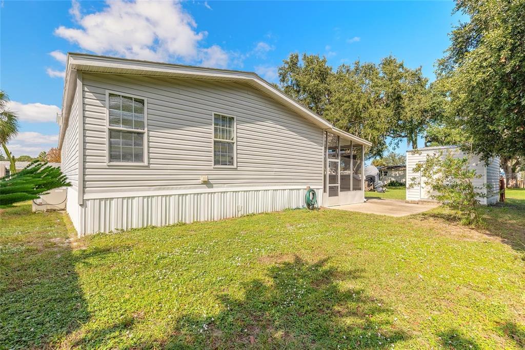The exterior of a light-gray mobile home features a screened-in porch and a small shed — 152 RED BASS LANE, EDGEWATER, FL
